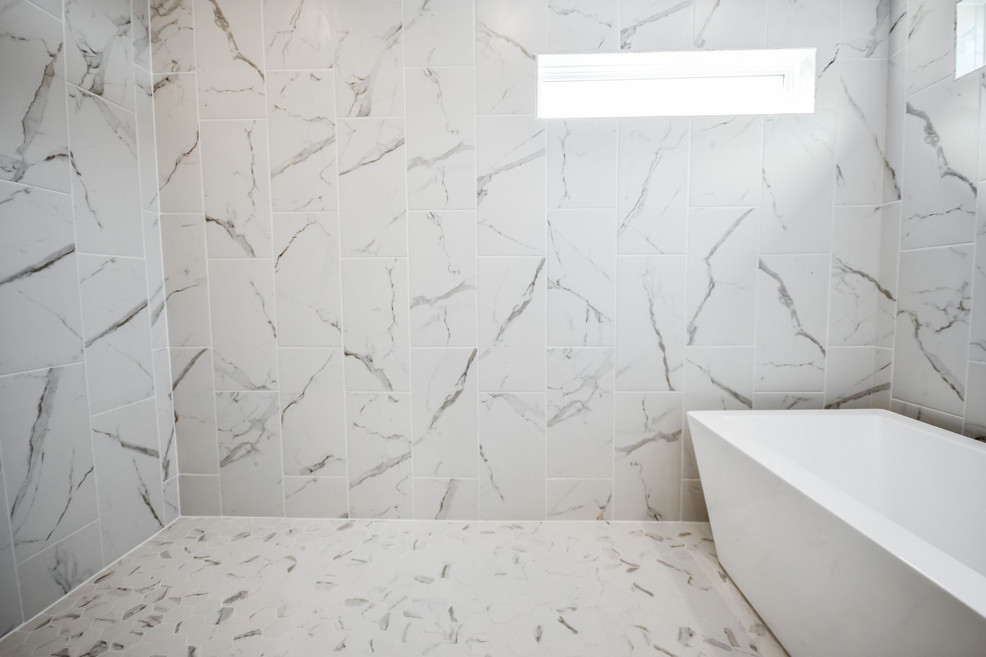 Bathroom with white marble-like tile walls and floor, a white rectangular bathtub, and a rectangular light fixture.