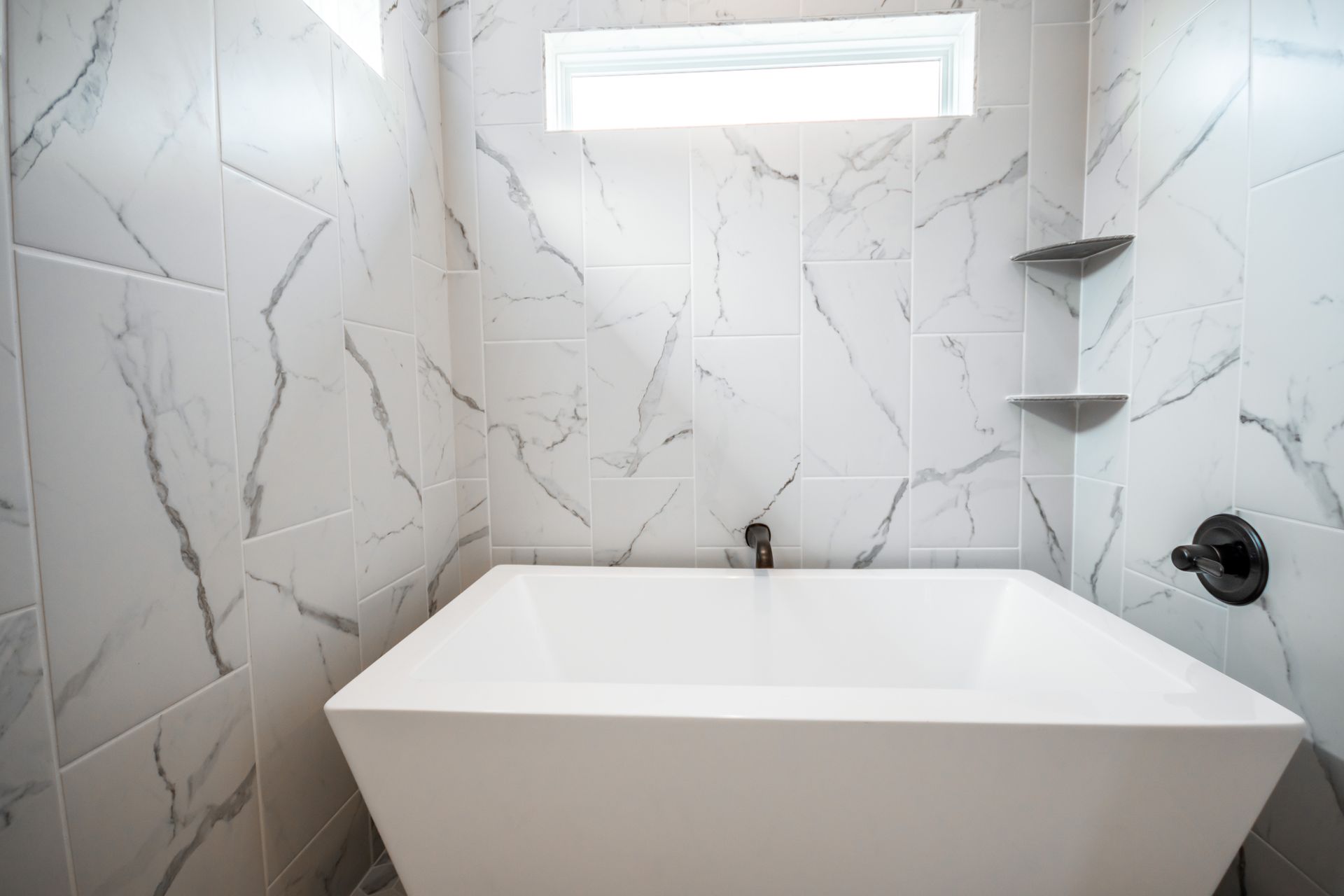 Modern white bathroom with a square tub, marble-patterned walls, and black fixtures.