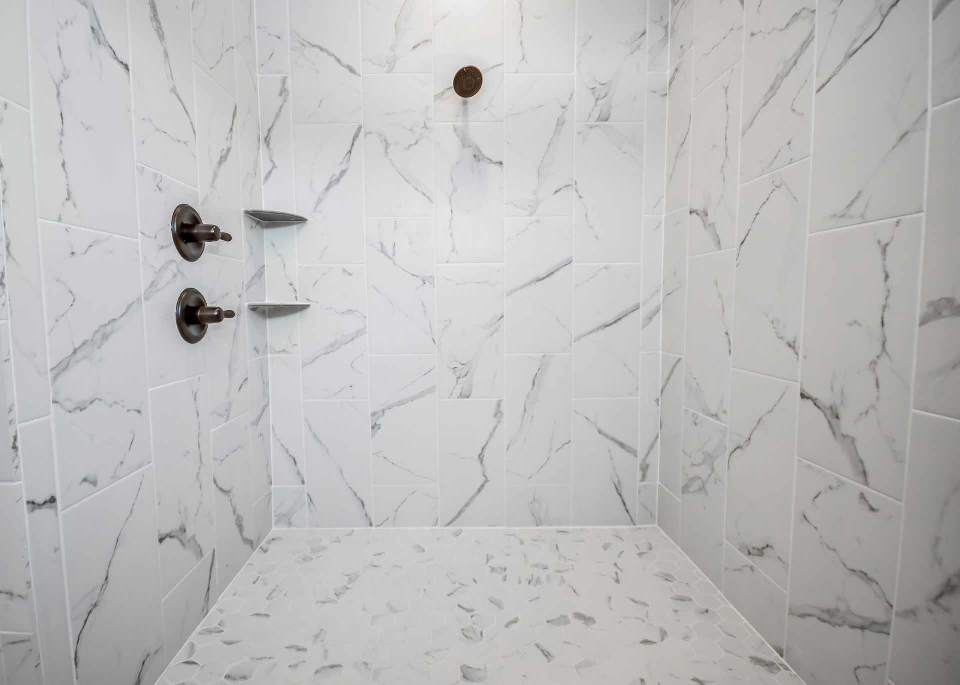 White tiled shower with bronze fixtures and a built-in bench.