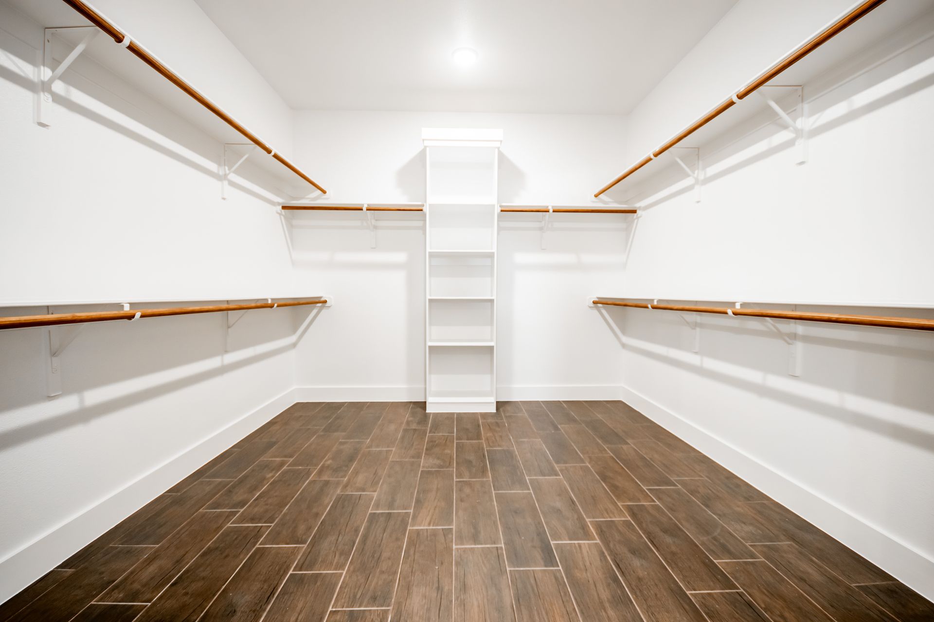 Empty walk-in closet with white walls, wooden shelves, and dark wood-look tile flooring.