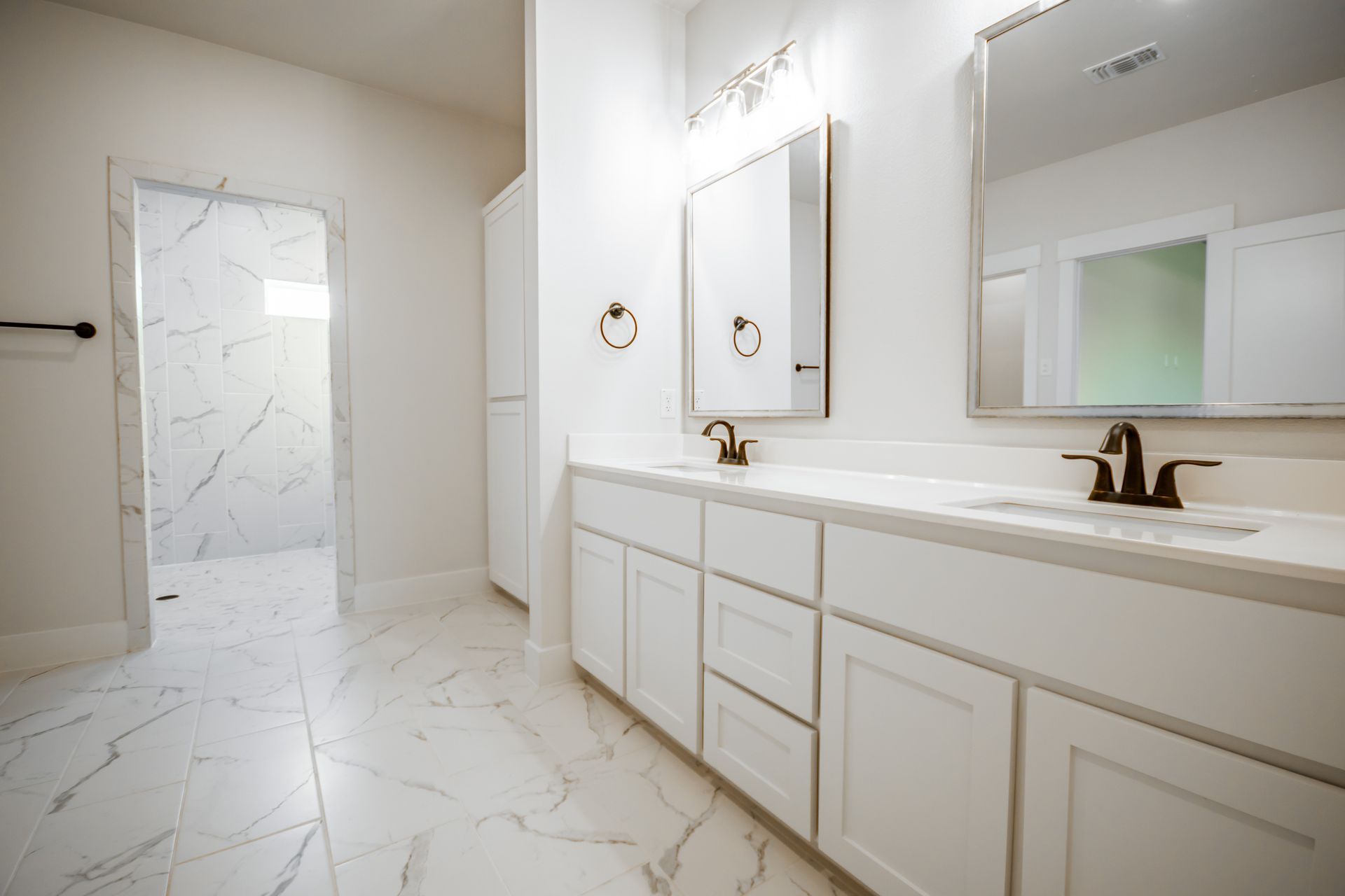 White bathroom with marble floor, double vanity, and walk-in shower.