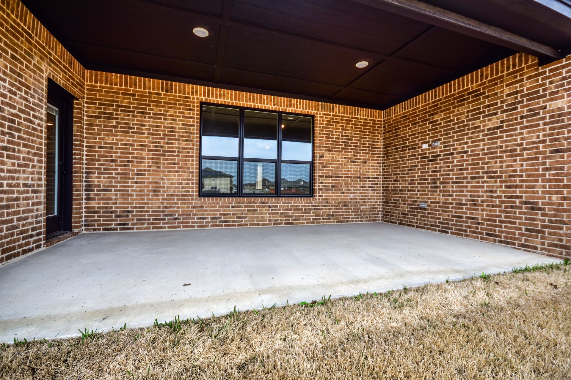 Covered brick patio with concrete floor, a window, and brown ceiling.