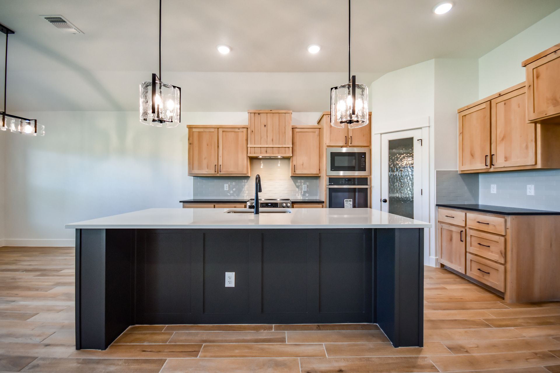 Modern kitchen with dark island and light wood cabinets, pendant lights.