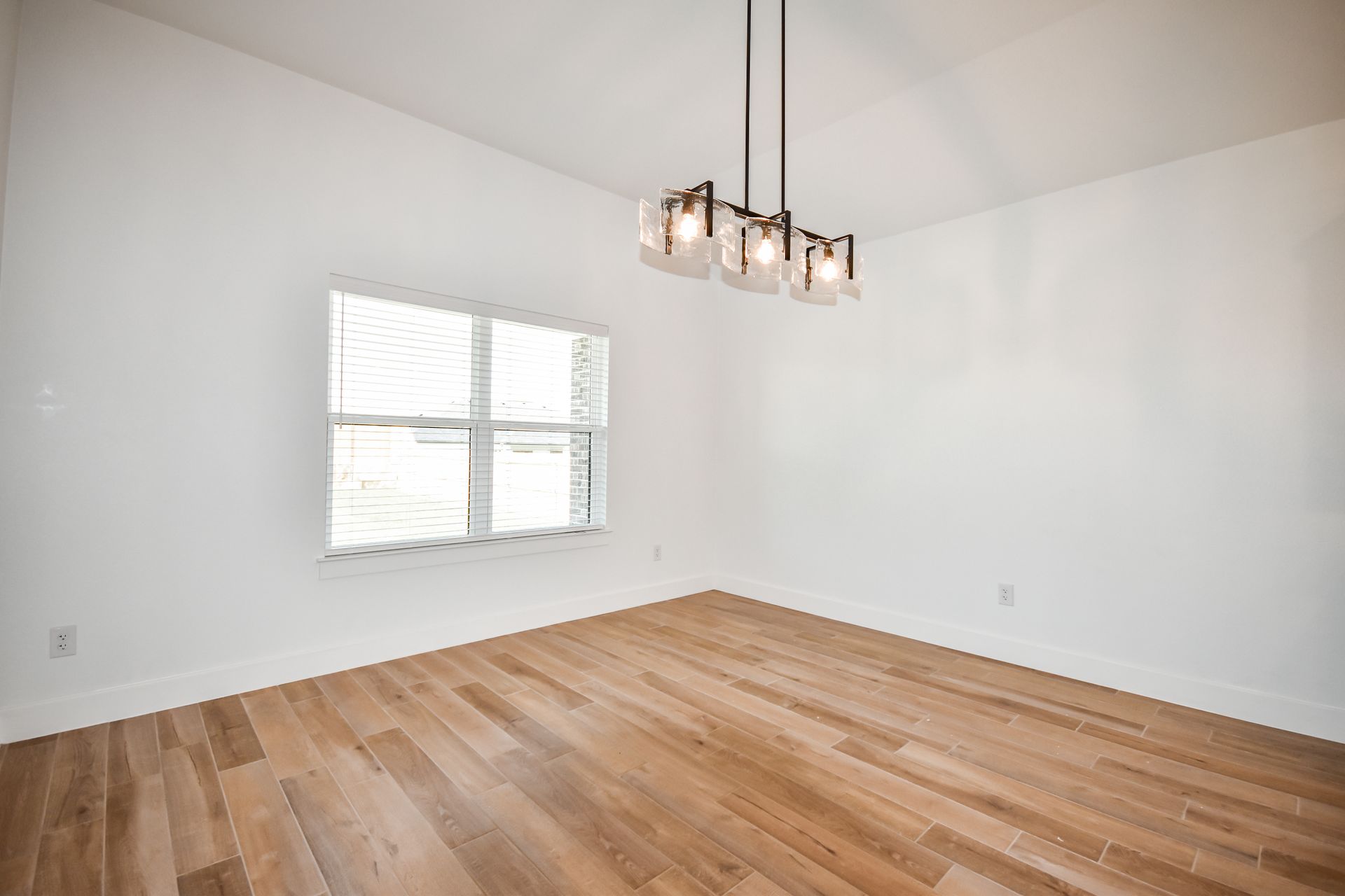 Empty dining room with wood floor, white walls, window, and pendant light fixture.