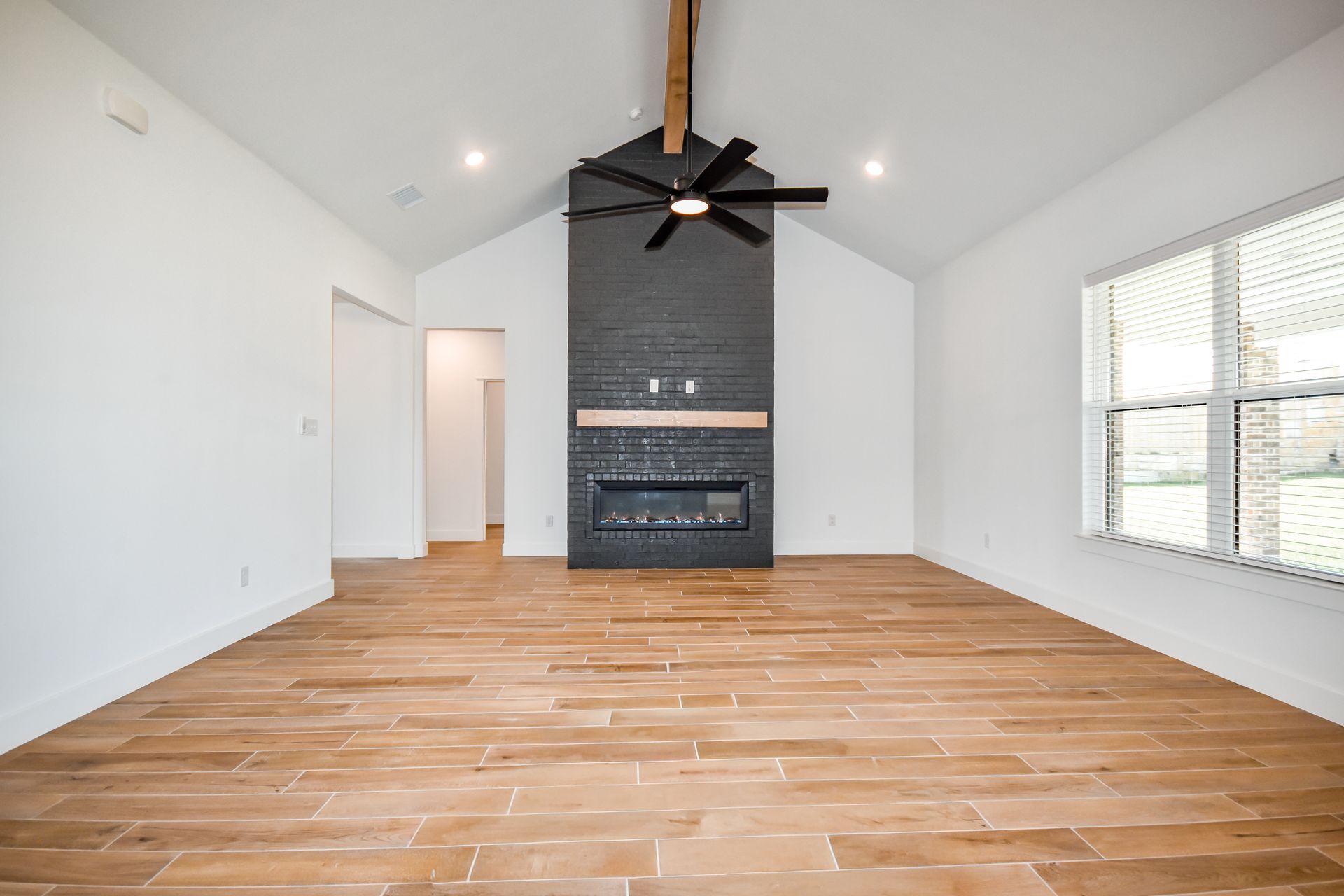 Spacious living room with a black fireplace, wood floors, and a ceiling fan.