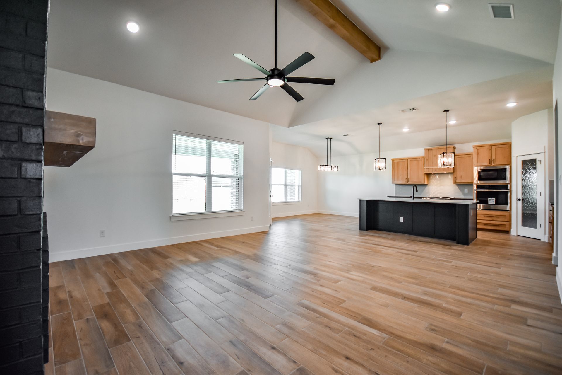 Spacious, open-concept living area with wood floors, vaulted ceiling, and dark accent island in kitchen.