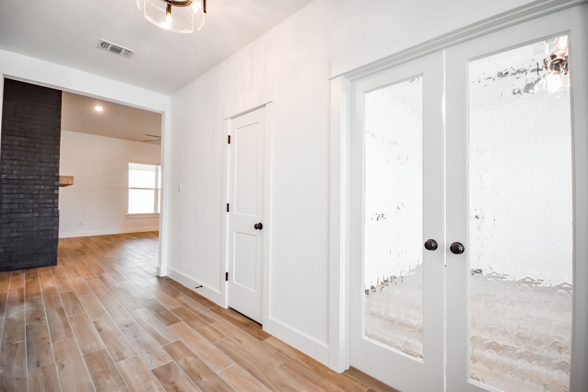 Hallway with hardwood floor, white walls, closet door, and glass-paneled double doors.