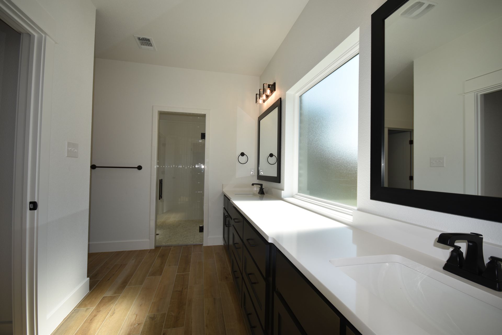 Spacious bathroom with a long vanity, large mirrors, and a glass-enclosed shower; bright lighting.