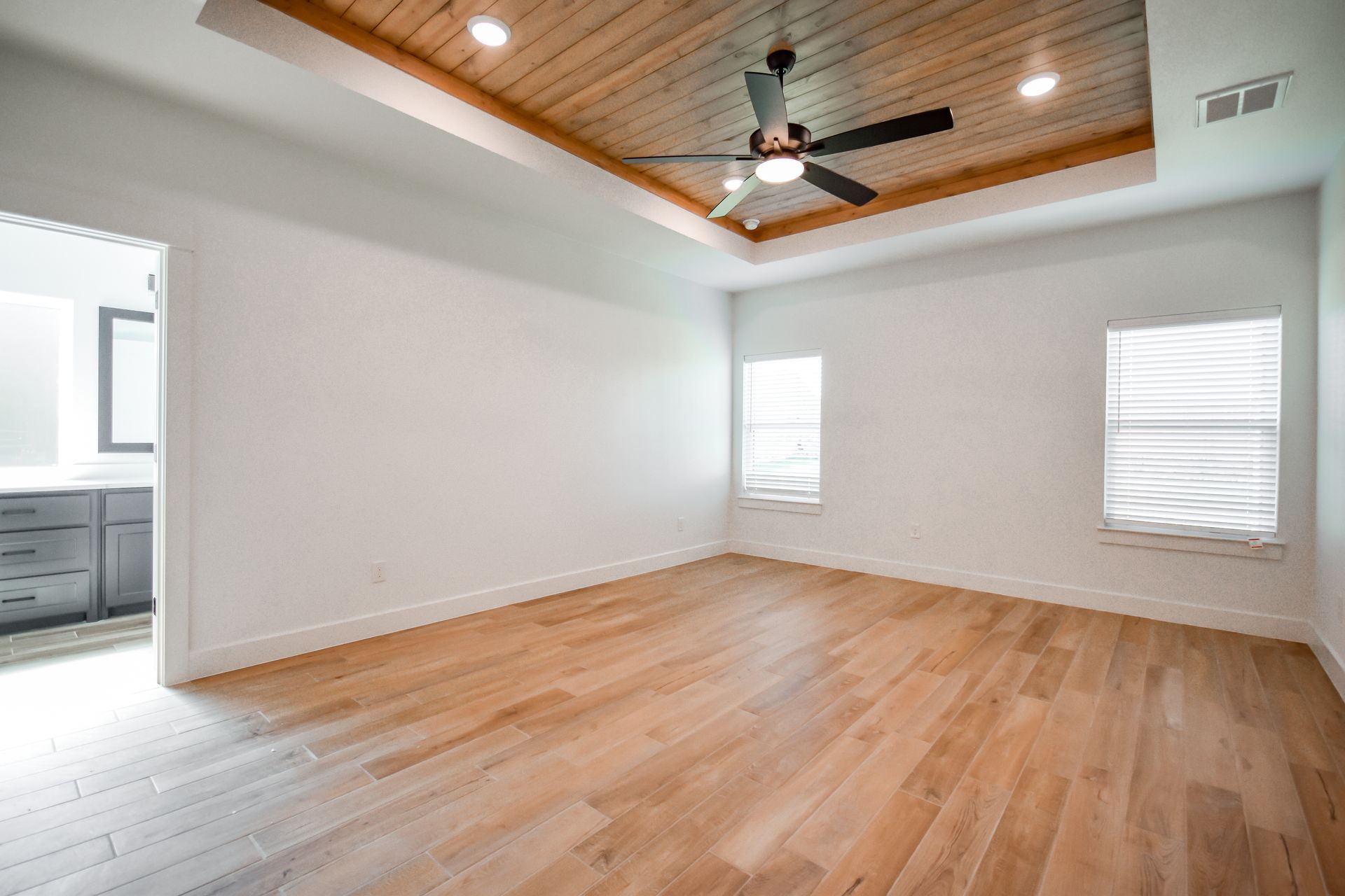 Empty bedroom with wood flooring, white walls, and a wooden ceiling.