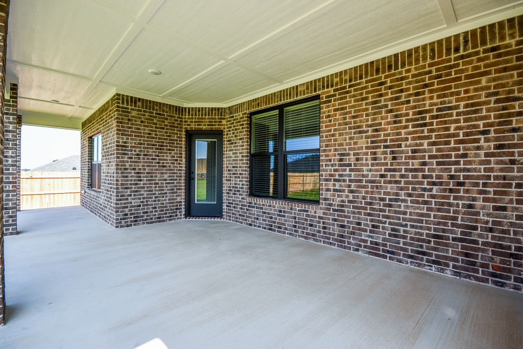 Covered patio with brick walls, a concrete floor, and black-framed windows and door.
