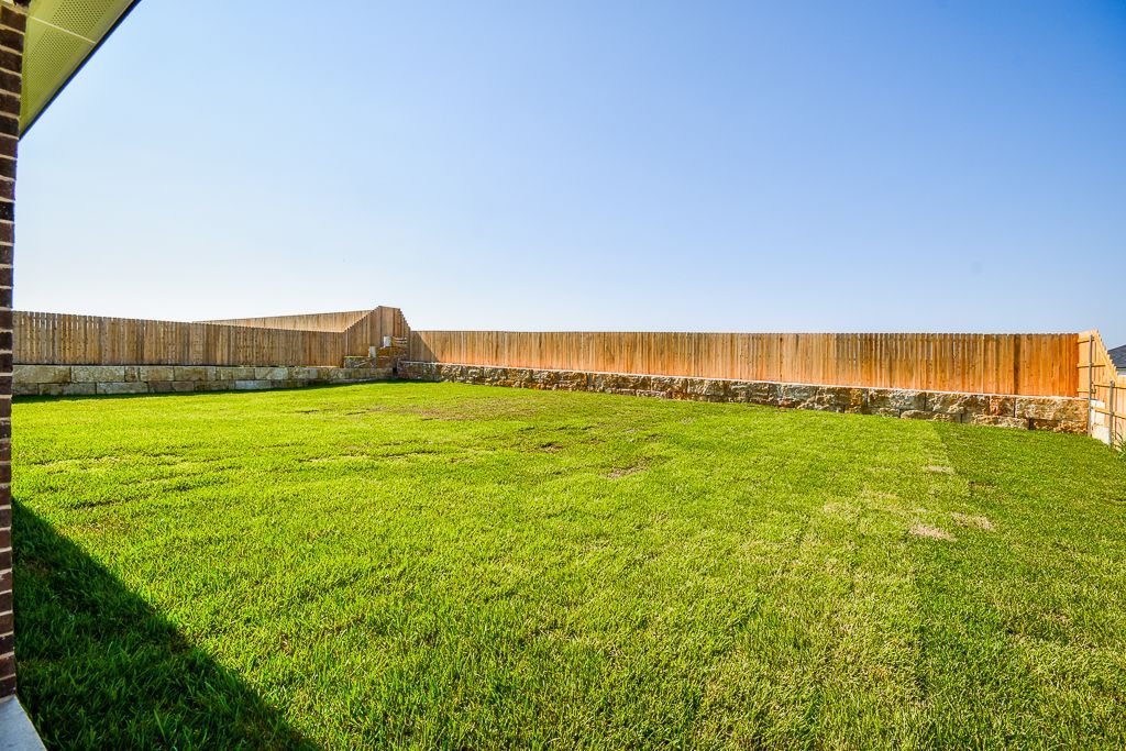 Green lawn enclosed by wooden fence under a clear blue sky.