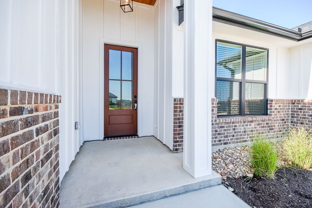 Front entrance of a modern house, with brown door, white siding, and brick accents.