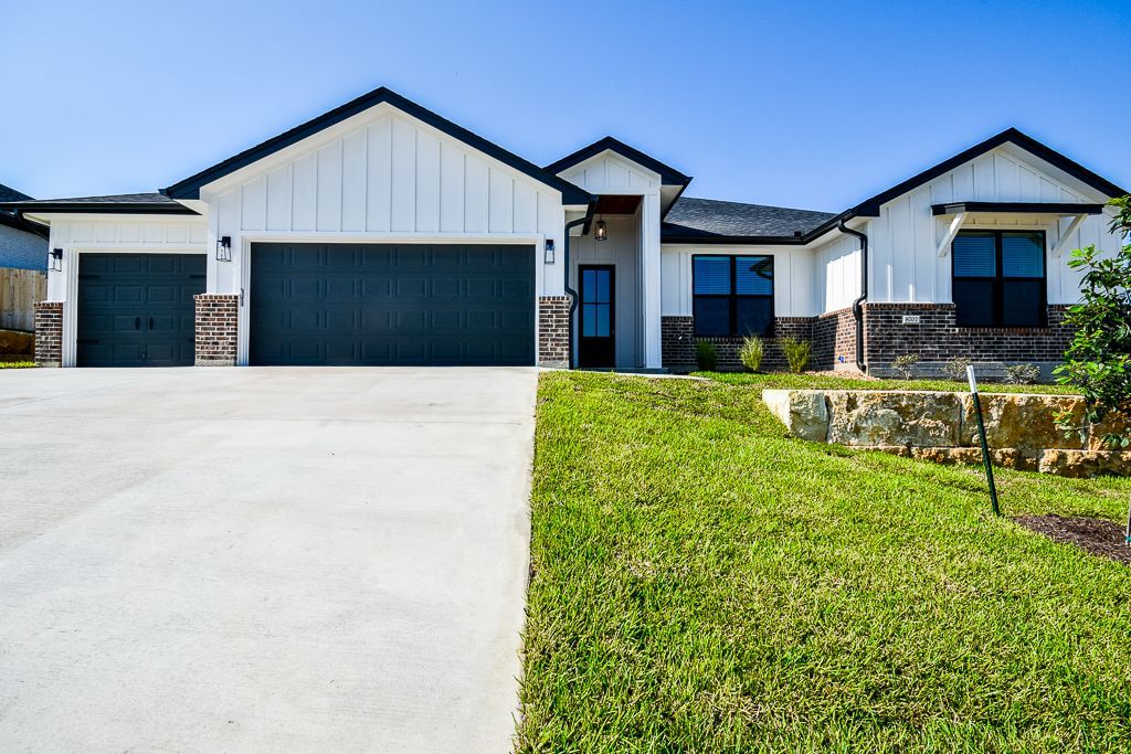 Modern white house with dark garage doors and a sloping green lawn.