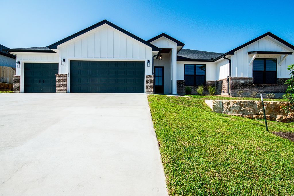 Brick and white house with attached garage and dry brown grass yard.