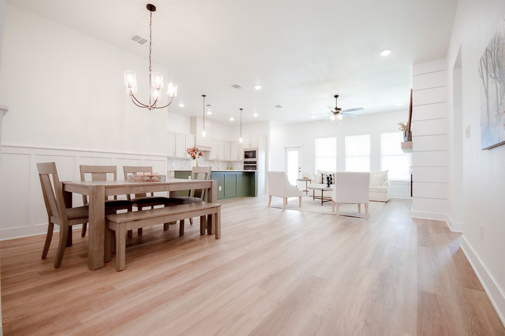 Open-concept dining and living area with hardwood floors, a wooden table, chairs, and a kitchen in the background.