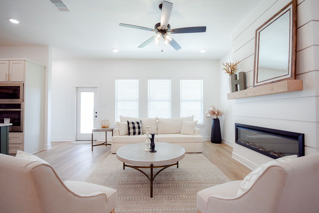 Spacious, bright living room with white furniture, fireplace, and large mirror. Neutral tones, modern decor.