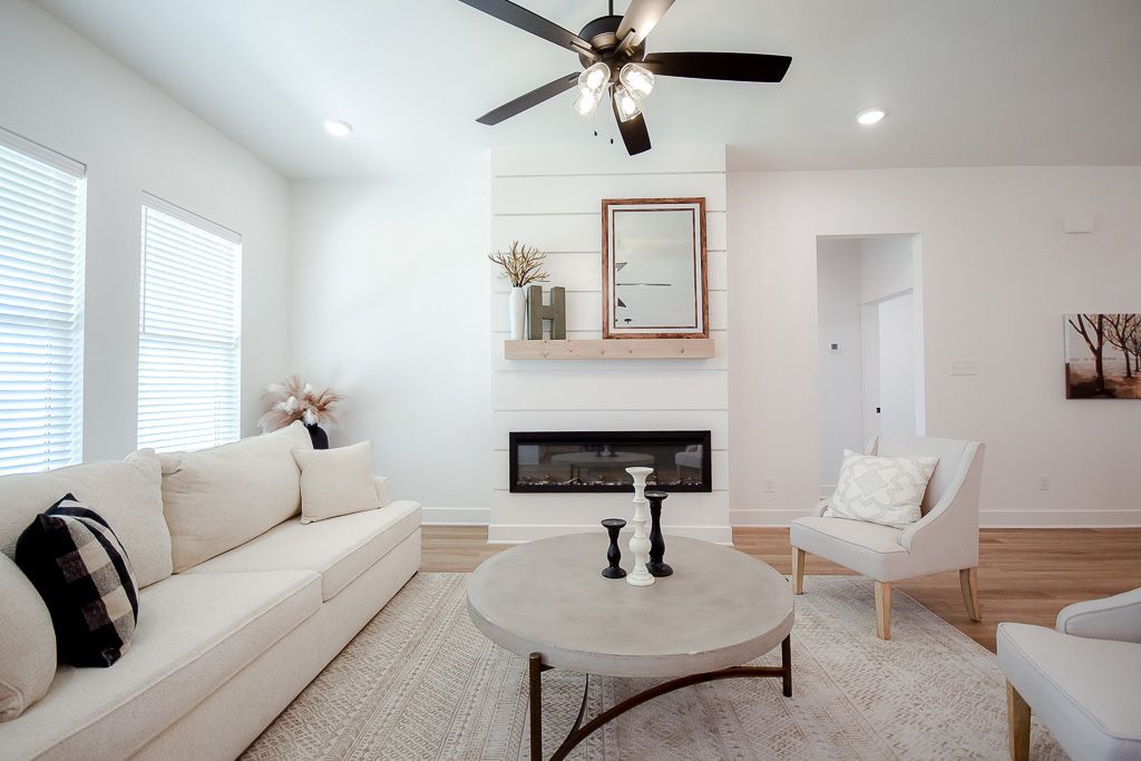 Bright living room with white sofa, armchairs, and round coffee table. Fireplace with mirror.