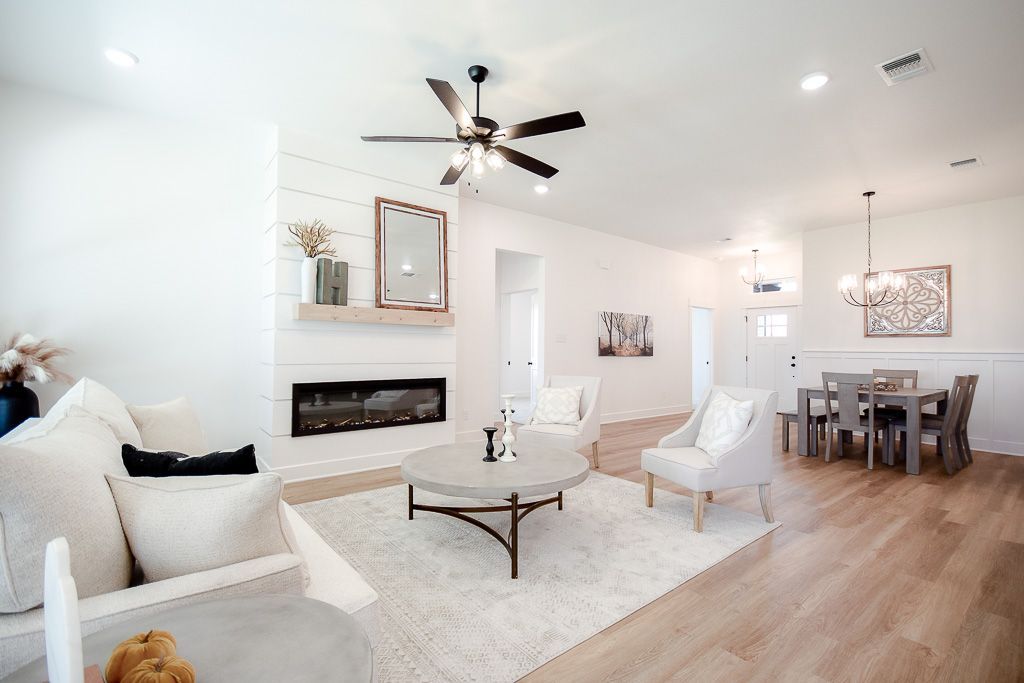 Bright, airy living room with fireplace, seating area, and dining space. Light wood floors, white walls.