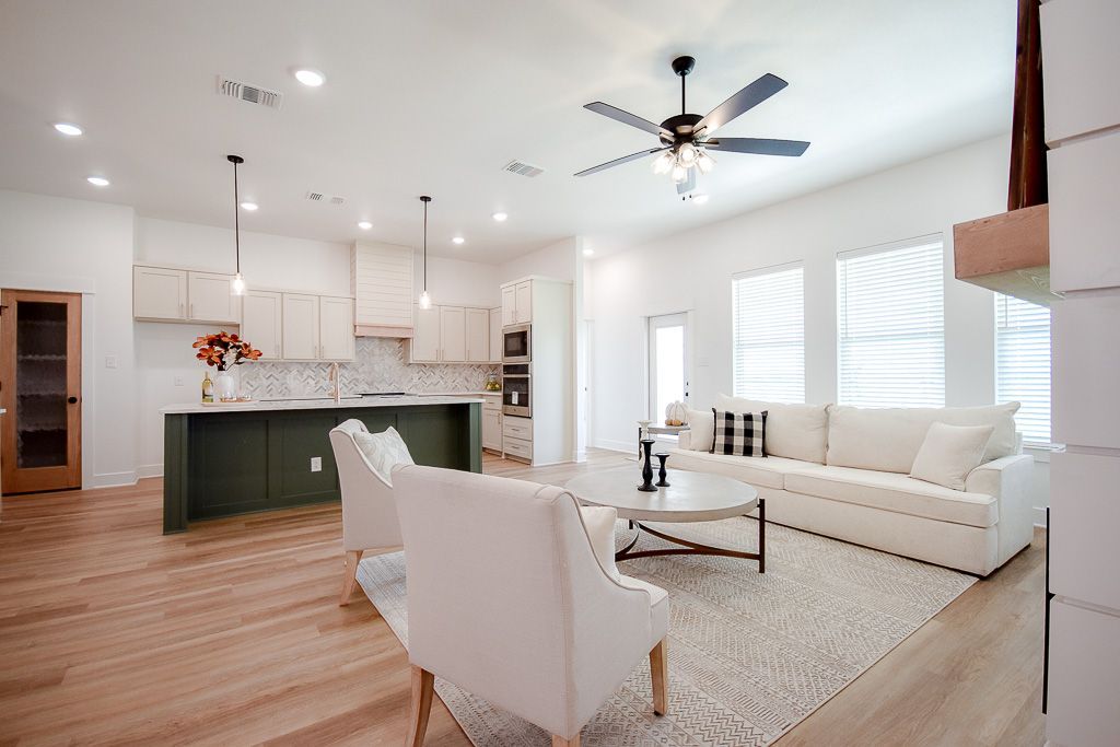 Open-concept living space with white walls, kitchen, living room with white sofa, chairs, and wood flooring.