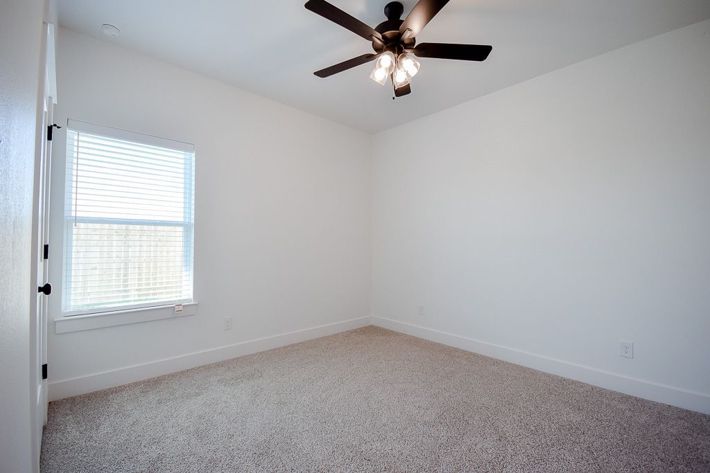 Empty room with white walls, carpeted floor, ceiling fan, and window with blinds.