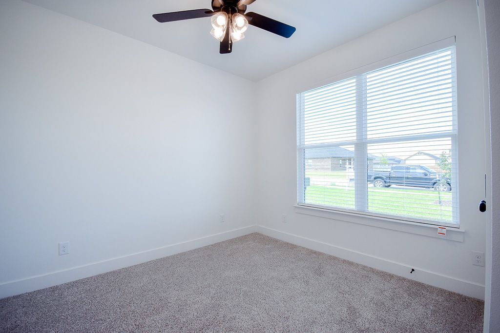 Empty room with beige carpet, white walls, and a window with blinds. Ceiling fan present.