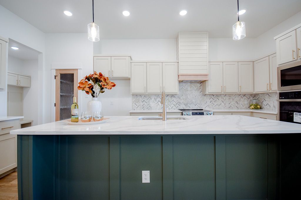 Modern kitchen with a dark green island, white cabinets, and a flower arrangement.