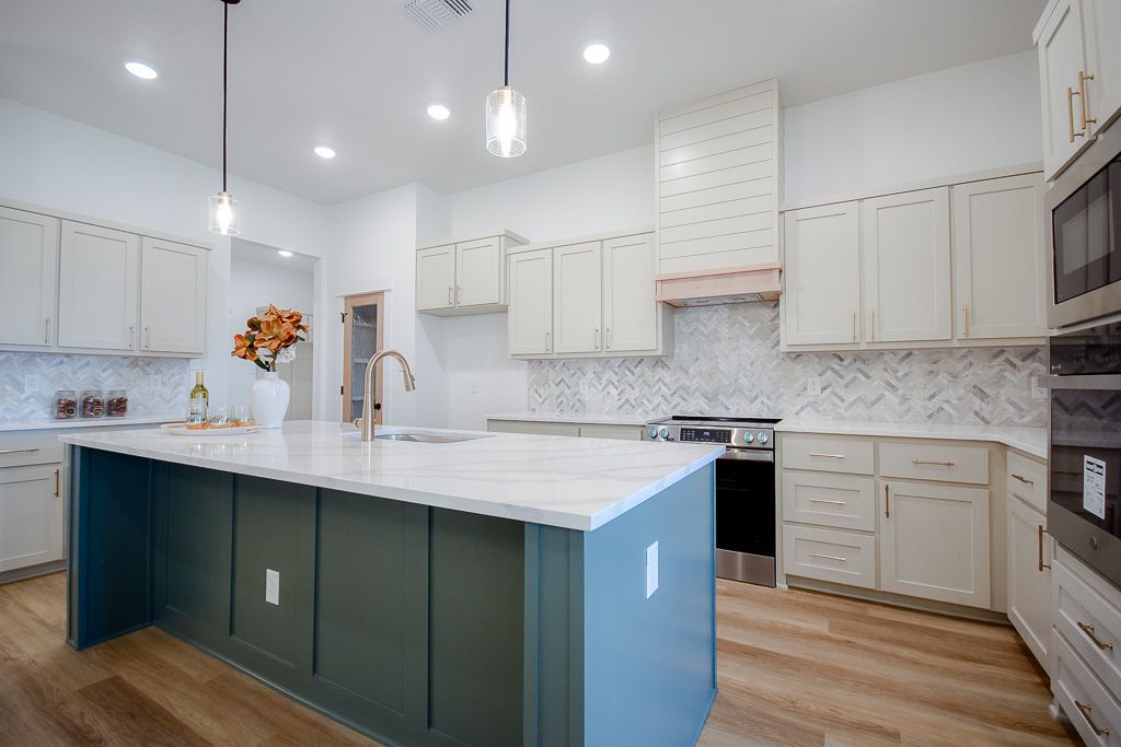 Modern kitchen with white countertops and cabinets, a teal island, and wood flooring.