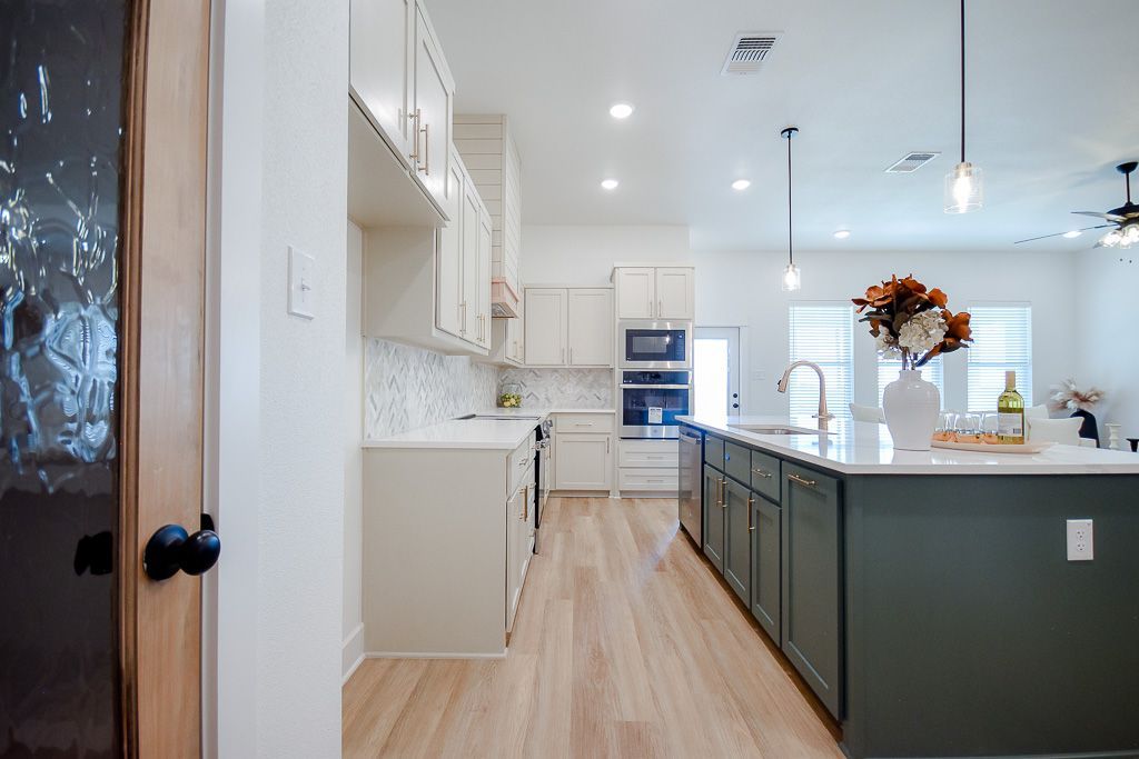 Modern kitchen with green island, white cabinets, and wood flooring.