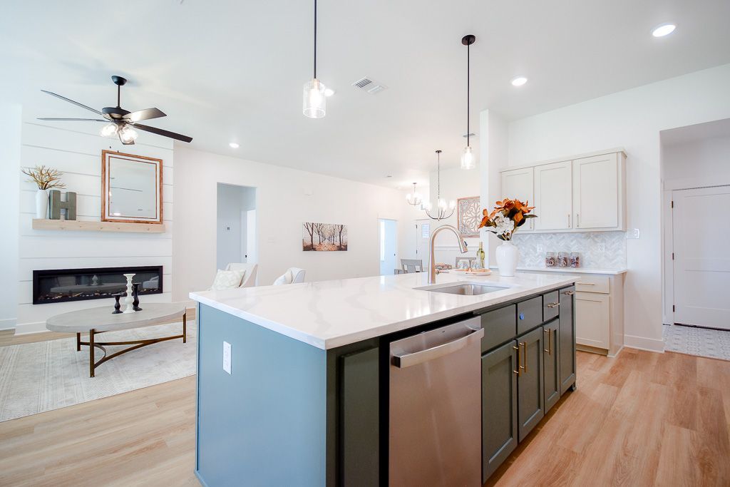 Kitchen with large island and fireplace, featuring white walls, green cabinets, and light wood floors.