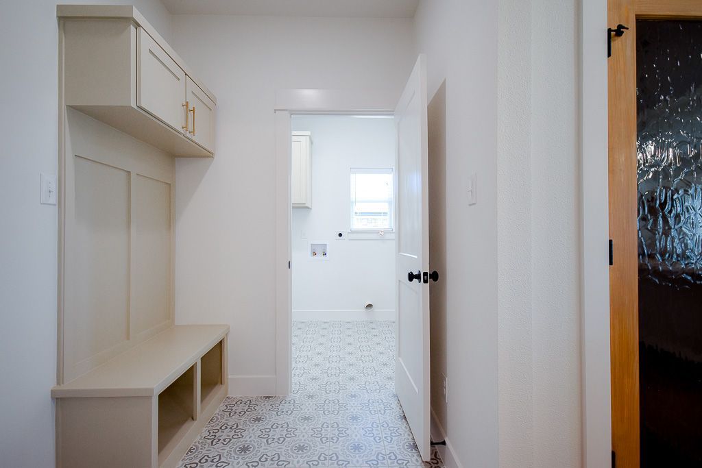 Hallway with a built-in bench, coat rack, and a view into a laundry room with patterned tile flooring.