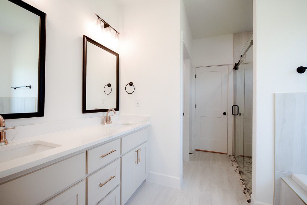 White bathroom with double vanity, mirrors, and a glass-door shower.