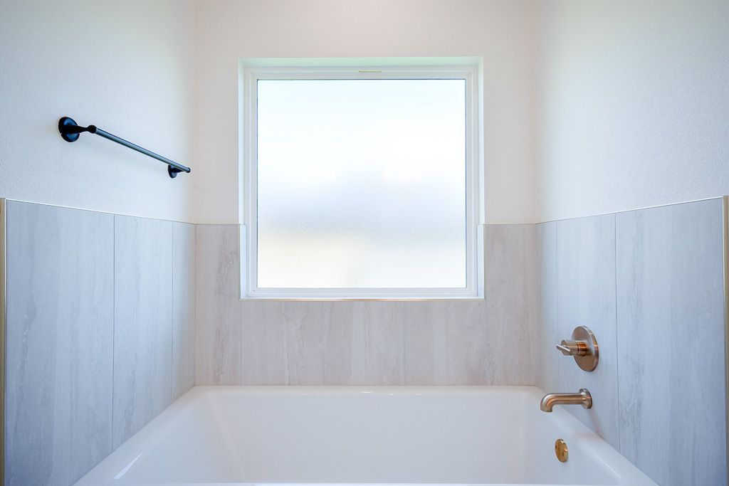 Bathroom with white bathtub, window, and wall tiles.