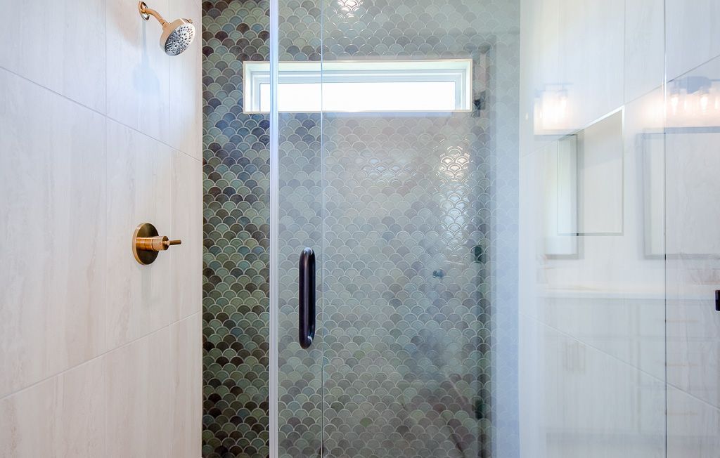 Bathroom shower with glass door and green mosaic tile accent wall. Gold fixtures.