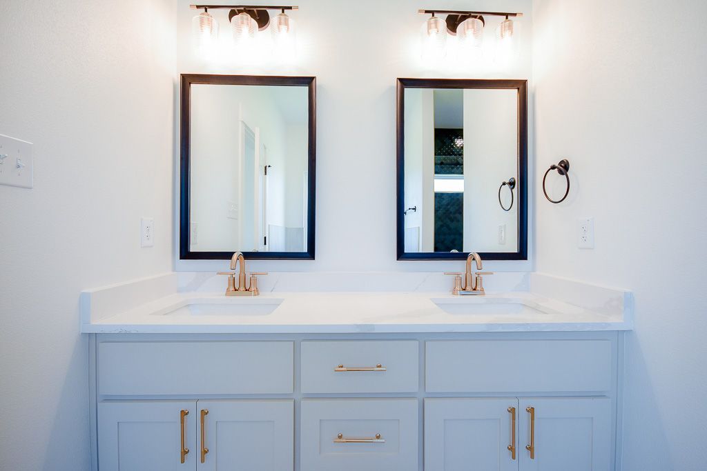 Bathroom vanity with two mirrors, gold fixtures, and gray cabinets.