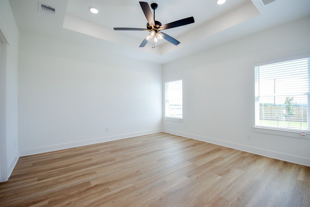 Empty, bright room with wood floor, white walls, two windows, and a ceiling fan.