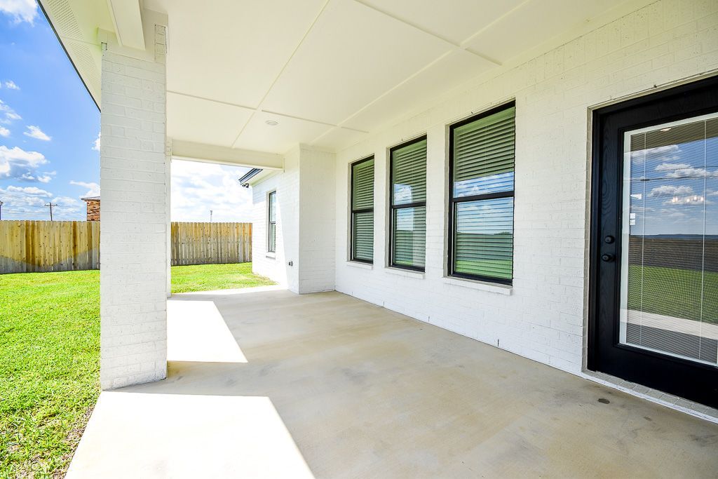 Covered patio with white stucco walls, concrete floor, black-framed windows and door, and a grassy backyard.