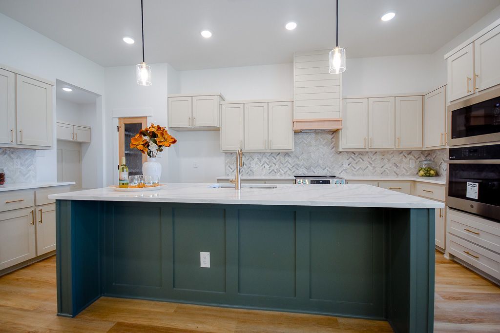Modern kitchen with sage green island, white cabinets, marble countertops, and wooden floors.