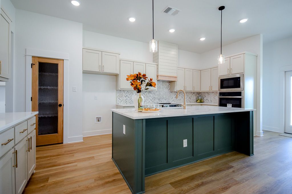 Spacious kitchen with a green island, white cabinets, marble backsplash, and wooden floors.