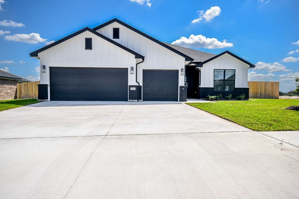 White house with black accents, two-car garage, large driveway, green lawn, against a blue sky with clouds.