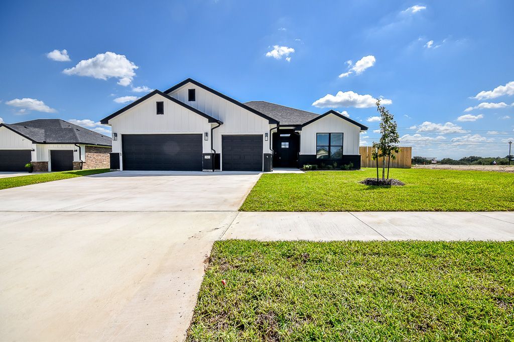 Modern white house with dark garage doors, bright blue sky, and green lawn.