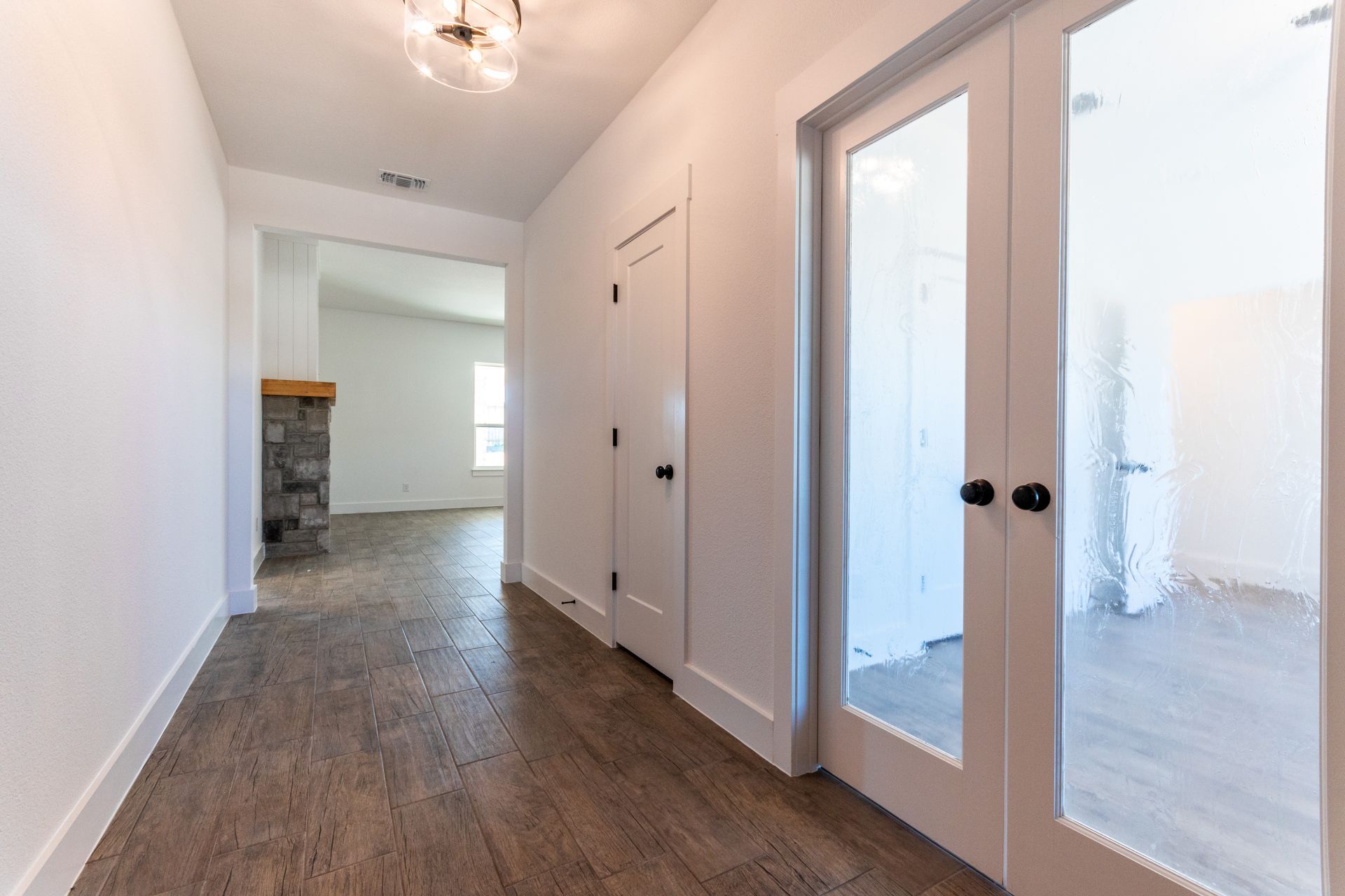 Hallway with white walls, wood floors, and French doors leading to a room.