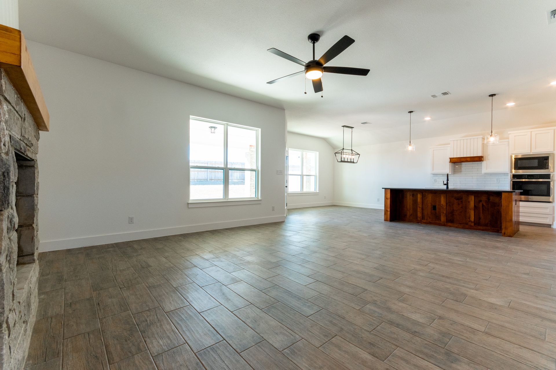 Empty living room with wood floors, fireplace, and open kitchen with dark wood island.