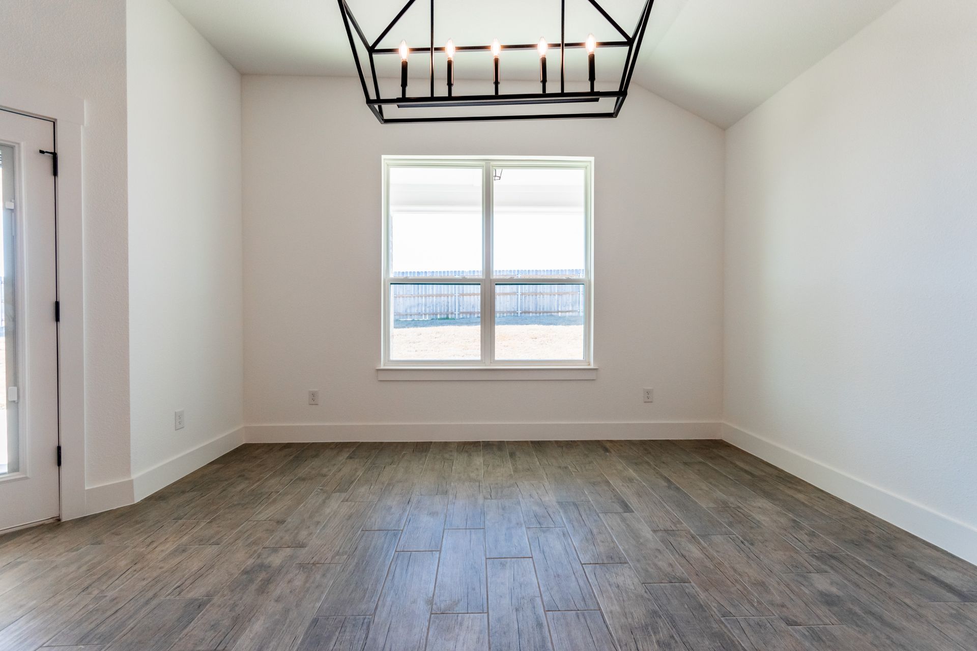 Empty room with gray wood floor, white walls, and a large window, contemporary light fixture.