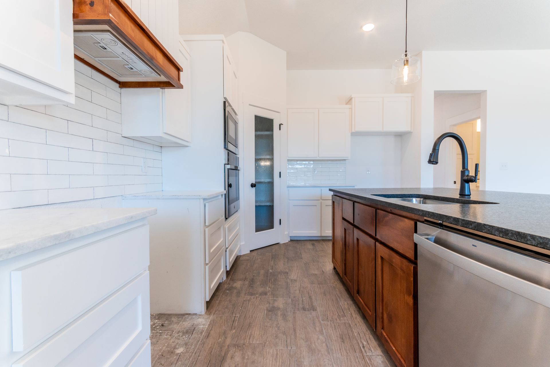 Modern kitchen with white cabinets, dark island, stainless steel appliances, and wood floors.