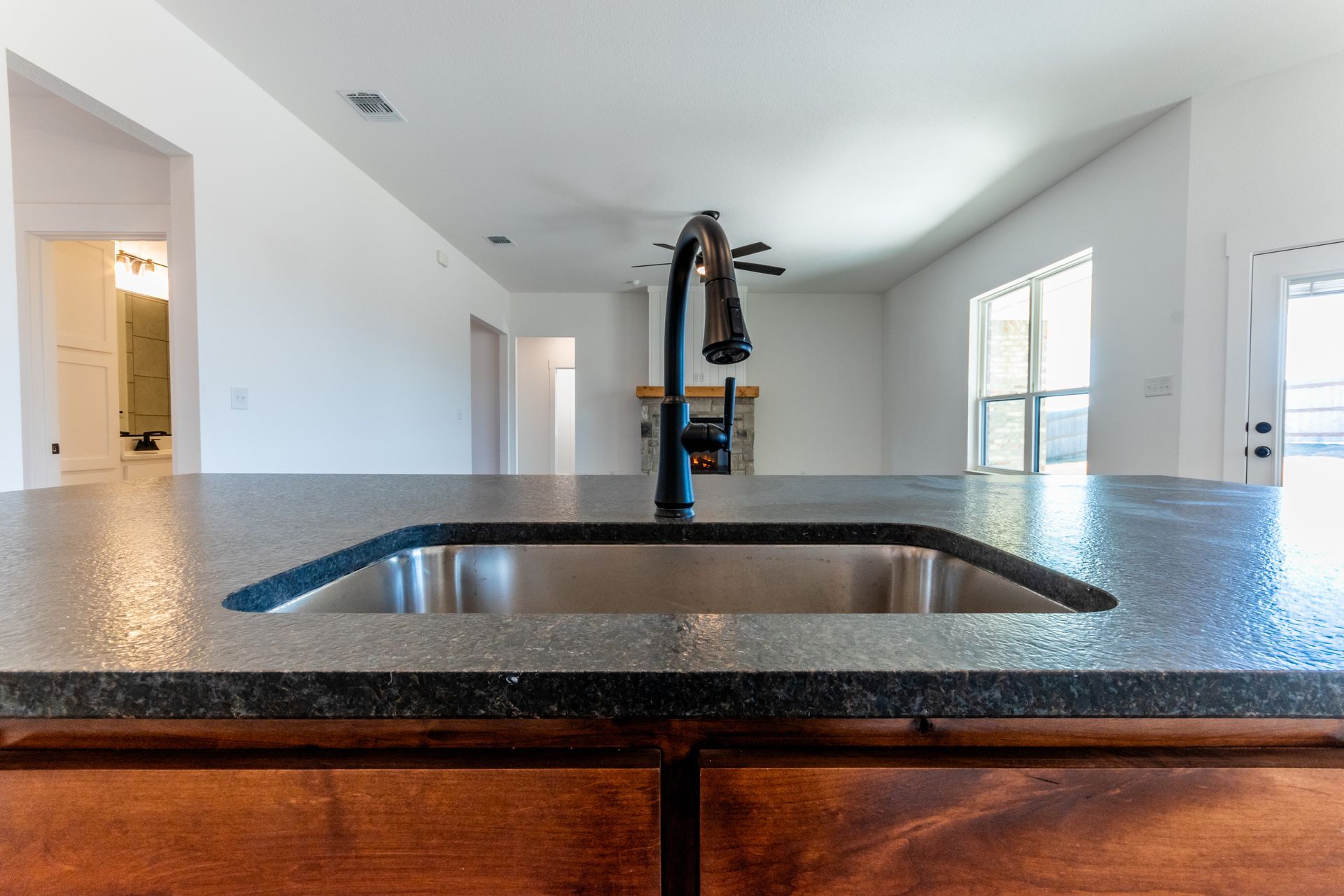 Kitchen island with sink, black faucet, and granite countertop, looking into a living space.