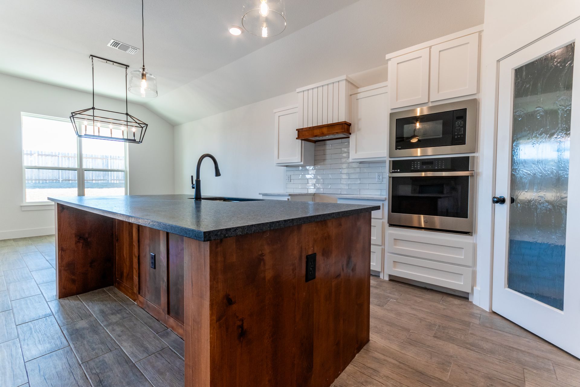 Kitchen with dark island, white cabinets, stainless steel appliances, and wooden floors.