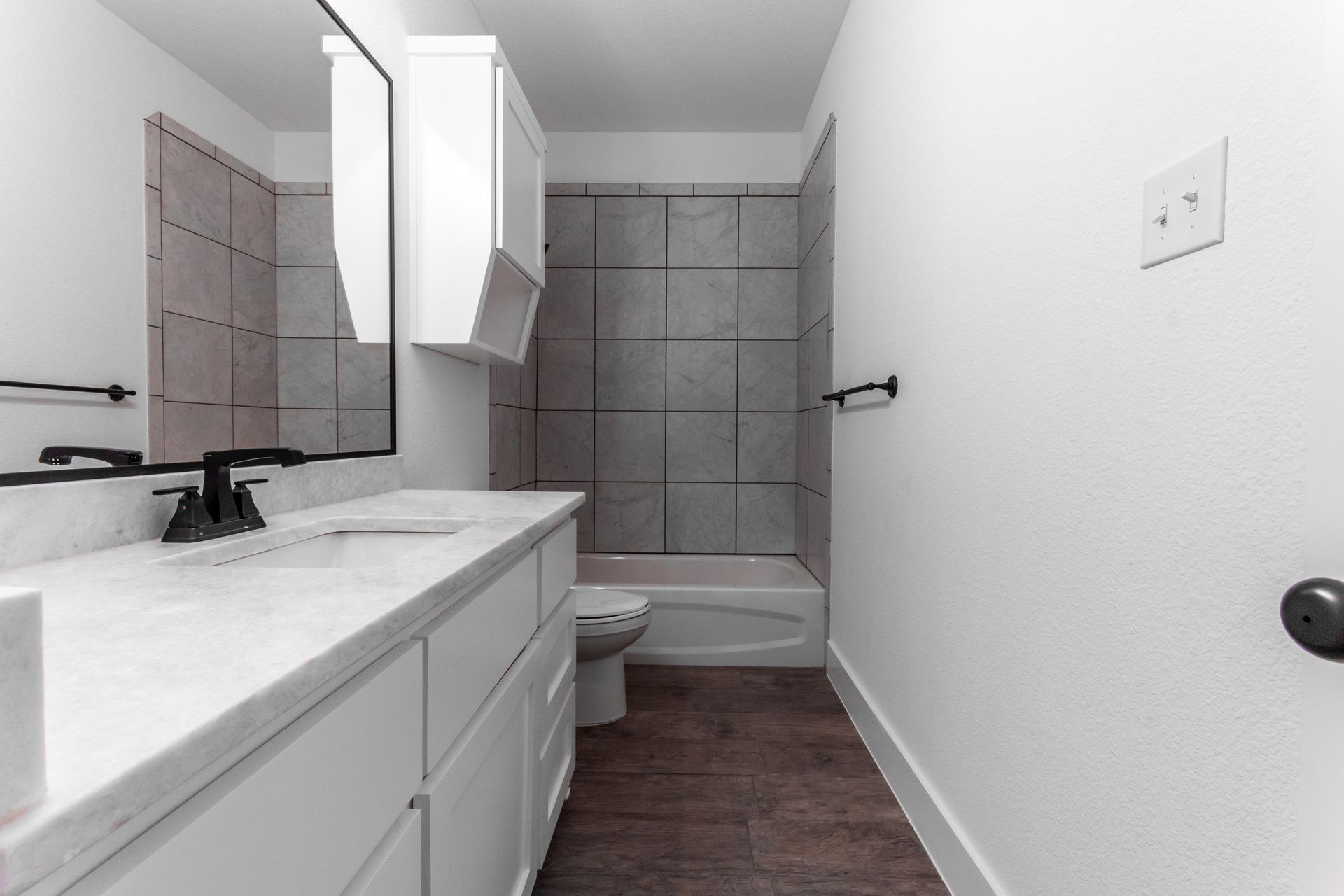 Bathroom with a white vanity, black fixtures, and gray tiled shower.