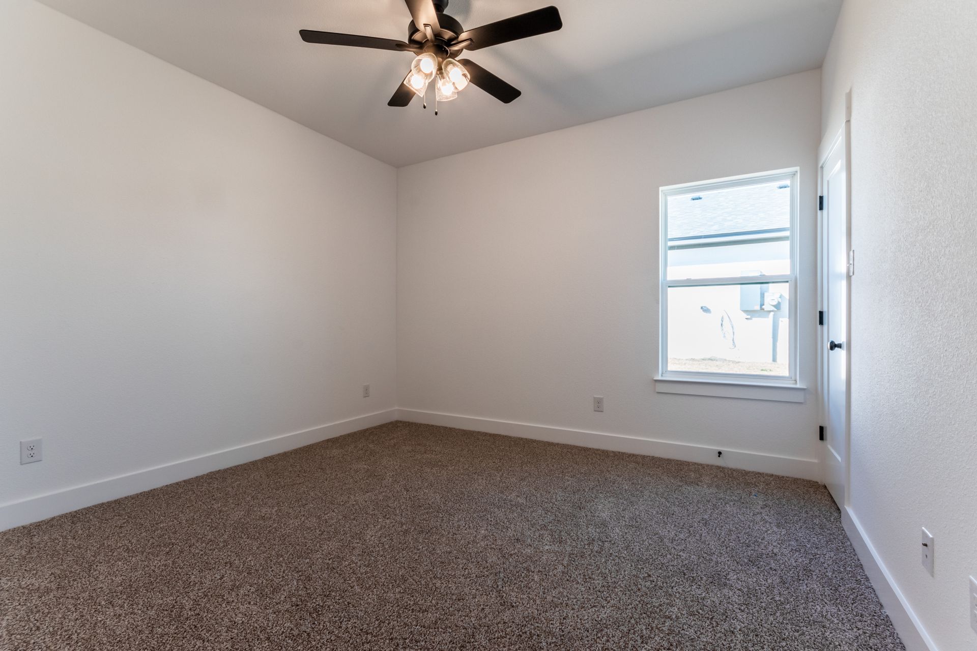 Empty room with white walls, brown carpet, window, and ceiling fan.