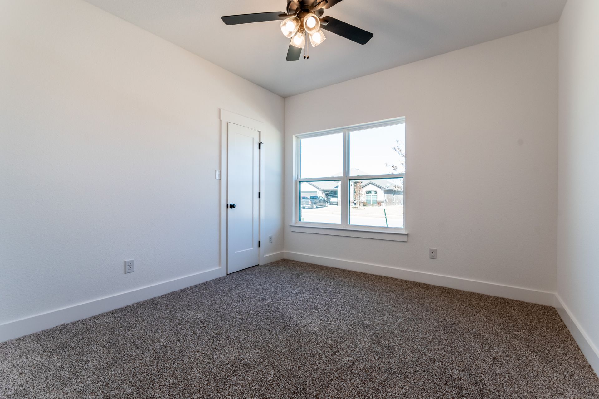 Empty room with white walls, window, and brown carpet. A ceiling fan is visible.