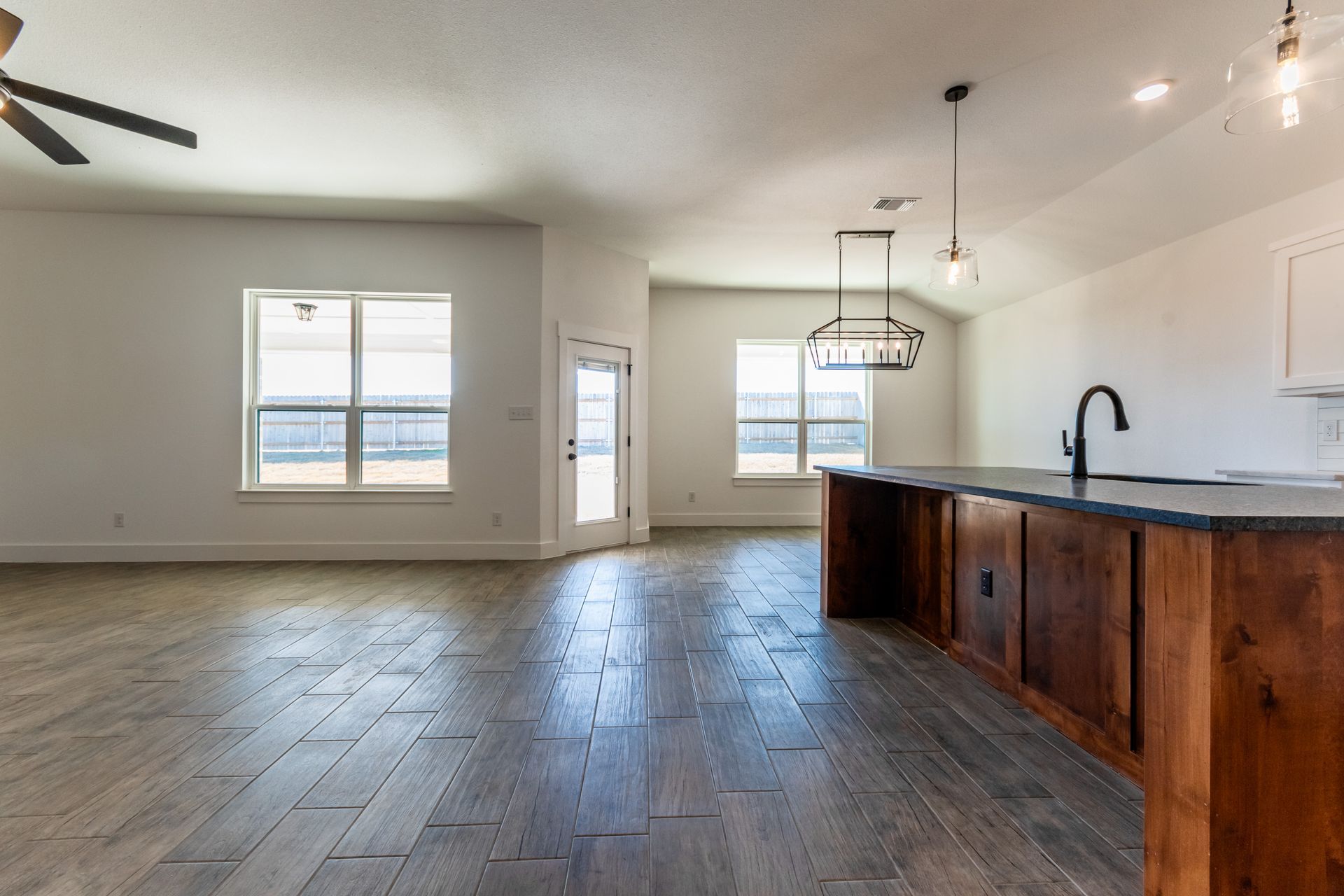 Spacious, empty living area with wooden floors, white walls, and a dark wood kitchen island.